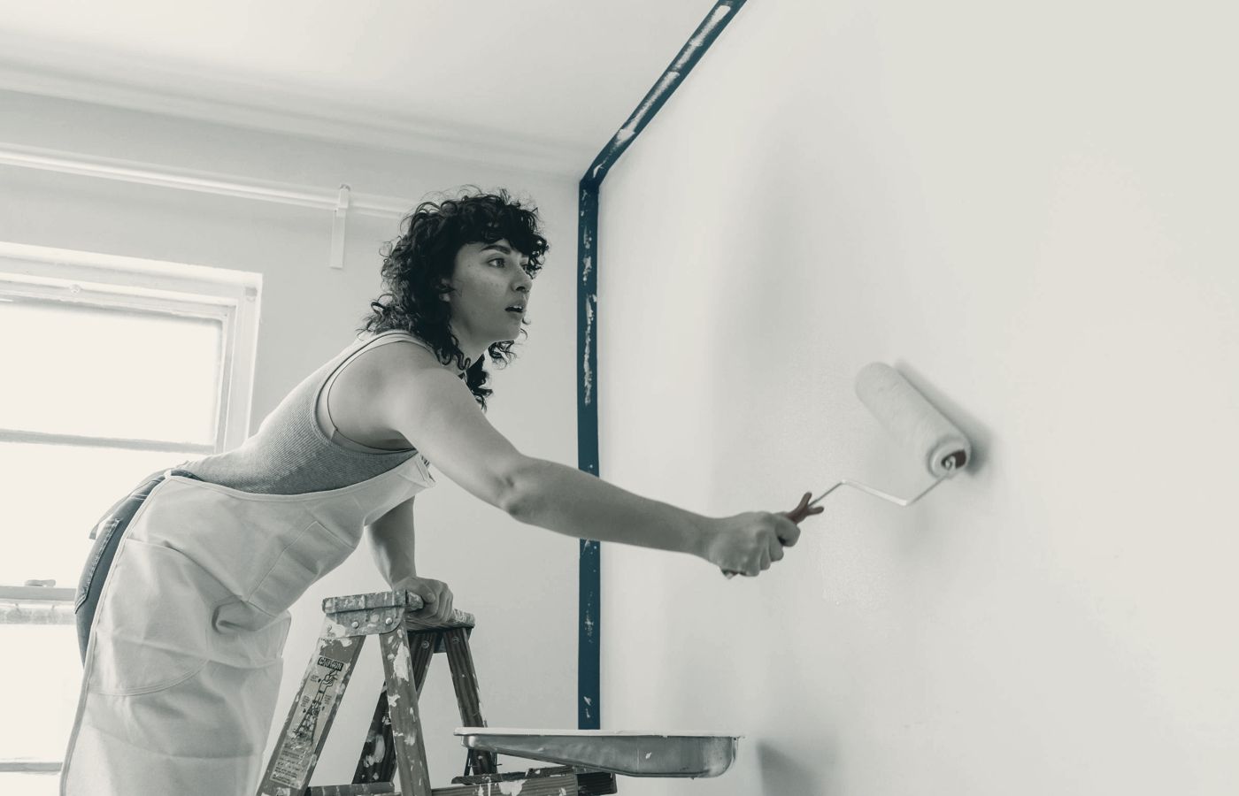 Painter on a stepladder rolling paint onto a wall